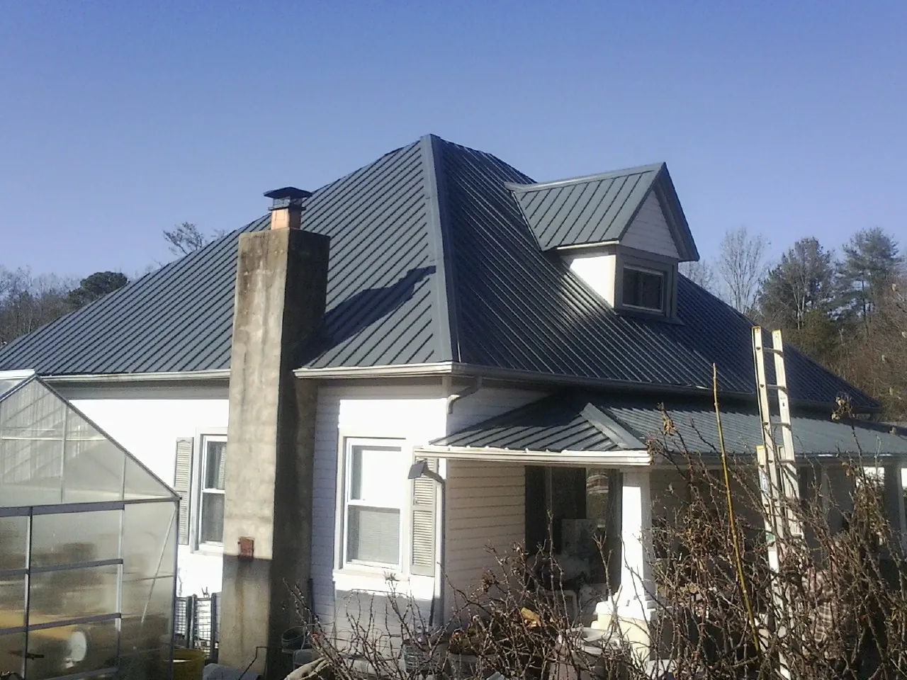 Dark blue standing seam metal roof on a white farmhouse with dormer — Slate & Tile Roof Repair by Roofing Brothers in Grand Mound