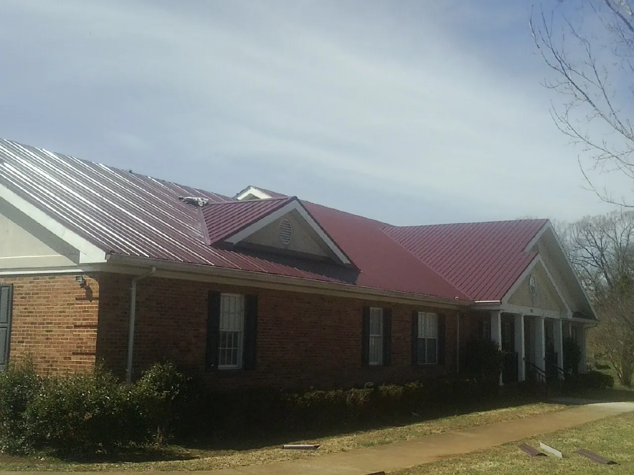 Red metal roof with gabled entries on a long brick building, from a Hail Damage Roof Repair job in Grand Mound