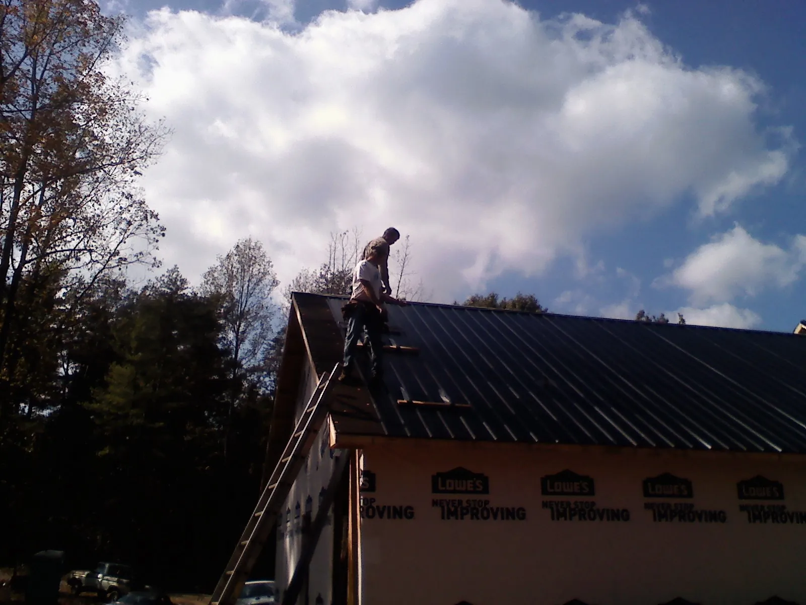 Roofer fastening dark metal panels high against a cloudy sky, from a Roof Inspection job in Grand Mound