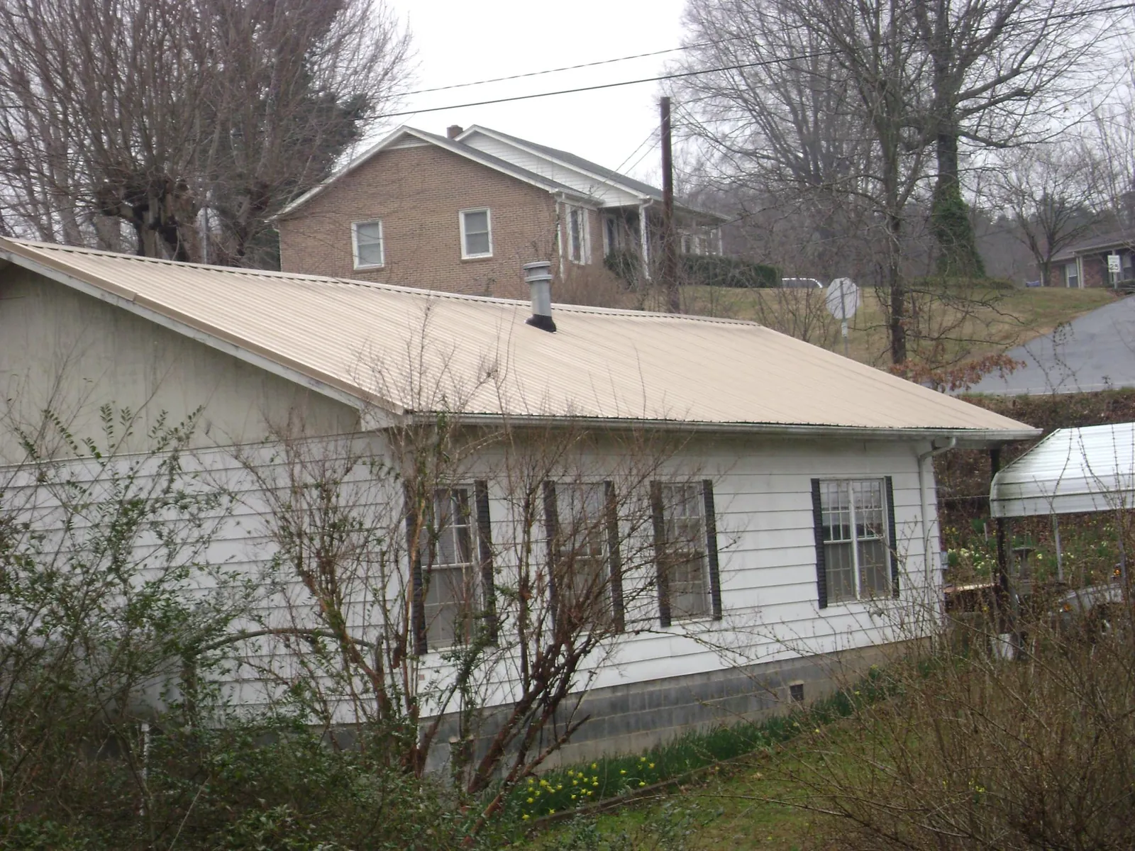 Tan metal roof on a white sided house set into a hillside — Commercial Roofing by Roofing Brothers in Grand Mound